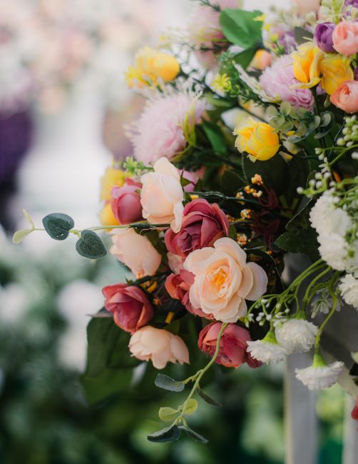 A vibrant floral arrangement featuring a mix of roses in soft peach and deep red hues, complemented by delicate pink and yellow blossoms, along with white filler flowers and lush green foliage. The bo