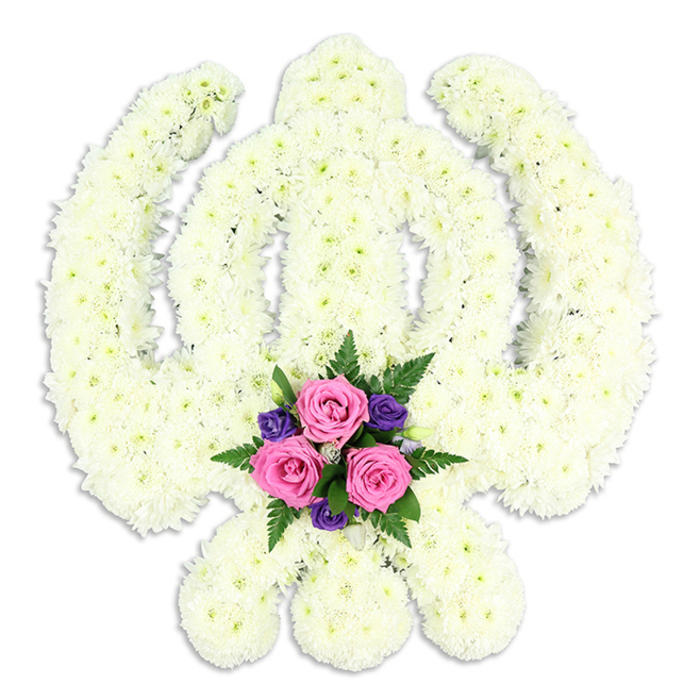 A commanding Sikh Khanda floral display stands front and centre, its sacred form captured in a beautifully detailed arrangement of white chrysanthemums set against a neutral white backdrop. The florist has shaped the central double-edged sword with crisp definition, its vertical line rising from the base of the piece and framed by the perfectly proportioned circle of the chakkar. On either side, the kirpans sweep outward and downward in elegant arcs, their outlines softened but not obscured by the dense covering of blooms. Each chrysanthemum head is small and carefully placed, giving the tribute a plush, almost quilted texture, with layered petals adding gentle movement and fine detail. The white of the flowers leans slightly towards creamy ivory in places, catching the light and giving the tribute warmth rather than starkness. Tucked at the bottom where the blades meet, a carefully composed cluster of accent flowers adds contrast and emotion. Three mid-pink roses sit prominently at the centre, their petals tightly layered in graceful spirals, accompanied by clusters of deep purple flowers that provide depth and richness. Sprays of fern and fresh green foliage frame this pocket of colour, suggesting life, continuity, and hope. A faint shadow beneath the tribute hints at its three-dimensional form and the sturdy frame supporting it, making the design feel substantial and enduring. This arrangement, suitable for Sikh funerals, cremation services, or memorial gatherings around Collier Row, Rise Park, and Mawney, would be placed close to the coffin or in a place of honour. It speaks simply yet profoundly of faith, respect, and the lasting presence of a loved one in the hearts of family and friends.