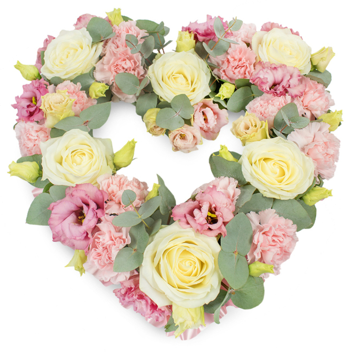 A detailed view of a heart-shaped funeral tribute is presented against a bright white background, the uncluttered setting allowing every pastel flower and leaf to be clearly seen, as though the arrangement has just been set down in a Collier Row chapel or family living room before a service. The heart is formed entirely from a tightly arranged mix of roses, carnations, lisianthus, and eucalyptus, creating a plush, continuous surface with a gentle, rounded silhouette. Large cream and pale lemon-ivory roses are prominent throughout, their petals soft and velvety, carefully spiralling from tight centres to open edges, offering a sense of peace and steady love. Clustered around and between these roses are light pink carnations, wonderfully ruffled, each one made up of many delicate petals that add volume and texture, like layers of shared stories and memories. To deepen the palette, the florist has tucked in richer mauve and magenta-pink lisianthus flowers, their more open, trumpet-like blooms giving a sense of airy grace and movement, preventing the heart from feeling too static. Small yellow-green buds can be seen nestled at intervals among the larger flowers, adding bright points of interest and a suggestion of new growth amid the sorrow. Running throughout the design, silvery-green eucalyptus leaves, with their smooth, roundish forms, weave in a gentle rhythm that traces the heart's outline and gives structure to the whole tribute. The result is an arrangement that feels both abundant and carefully composed, a fitting symbol of sympathy and remembrance for a loved one from the Collier Row area, entrusted to the hands of Collier Row Flowers to convey what words may not fully express.