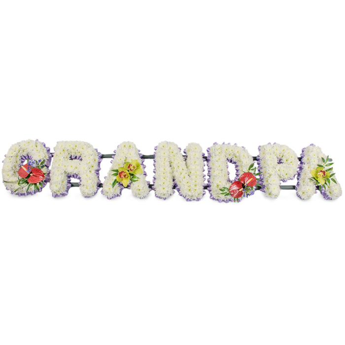 A carefully composed funeral flower tribute dominates the image, spelling out the word GRANDPA in seven sturdy, three-dimensional capital letters. Set on a clean white background, the letters appear almost to float, yet are clearly supported by discreet dark green bars that run behind them, indicating a design ready to be placed along the base of a coffin or at the head of a graveside. Each letter is lavishly covered with small, pristine white chrysanthemums, arranged so densely that very little of the underlying base can be seen. The overlapping petals create a rich, velvety texture, reminiscent of a soft blanket, offering a sense of comfort and serenity. A slim band of pale lavender ribbon traces the lower edge of every letter, giving a delicate lilac trim that frames the white flowers and adds gentle contrast.
Strategically placed accent sprays provide both visual rhythm and emotional emphasis. The first letter, G, and the central D are embellished with vibrant red anthuriums. Their glossy, heart-shaped forms and upright yellow spadices are cradled in deep green foliage, with fine touches of purple filler flowers peeping through, suggesting devotion and courage. The first A and the final A carry clusters of yellow-green orchids, whose graceful, intricate blooms rest lightly among the white chrysanthemums, symbolising admiration and enduring love. This interplay of crisp white, cool lavender, deep red, and fresh lime-green ensures the tribute feels both composed and heartfelt.
A piece like this would feel at home in a Collier Row farewell, perhaps at a service near White Hart Lane or Romford's outskirts, where families gather to honour a grandfather's life. It offers a clear, personal message in flowers, speaking gently of gratitude, remembrance, and the bond that remains.