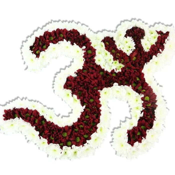 Rendered with meticulous floral technique, this Om (Aum) motif is a study in contrast and texture photographed against a stark white backdrop. The interior of the symbol - the distinctive '3'-like curve, the sweeping lower stroke, and the upper crescent with its bindu - is densely composed of dark maroon and burgundy chrysanthemum-like blooms; these small-headed flowers are so closely set their combined petals form a plush, velvety surface, while the small lime-green disc centres peek through to create subtle tonal variety. Encircling the symbol and filling its inner negative shapes is a thick, undulating edging of immaculate white spray chrysanthemums, chosen for their delicate scale and ability to read as a clean, architectural outline against the saturated red. A faint drop shadow grounds the arrangement visually, emphasizing the work's three-dimensional, sculpted quality as if it were resting on a white pedestal in a studio on Collier Row Road. The touch of scent is muted and comforting - a cool, green chrysanthemum note rather than overt perfume - and the petals would feel silky and slightly cool to the fingertips. This composition is the kind of floral tribute commissioned for meditation spaces, cultural ceremonies, and respectful memorial displays across Havering and nearby Gidea Park: restrained, respectful and meticulously arranged so that the sacred symbol communicates both artistry and devotion without distraction.