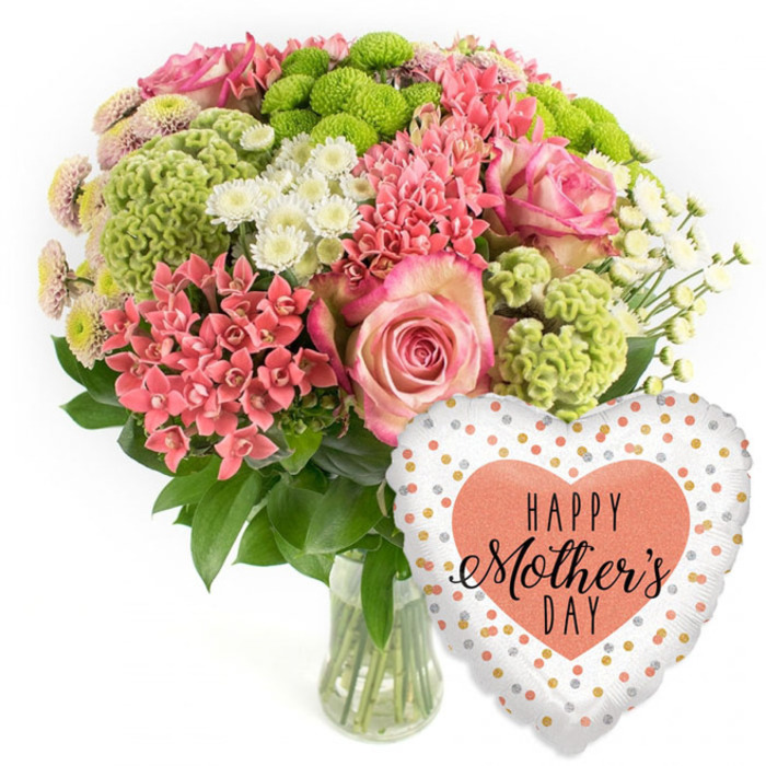 Against a clean white background, this Mother's Day floral display feels fresh and modern, like a product photograph ready for a Collier Row Flowers online gallery. The main focus is a rounded bouquet in a clear glass vase, placed slightly to the left of the frame so there is space for the coordinating balloon. The vase is plain and transparent, allowing the viewer to see the straight green stems and the clarity of the water, which emphasise the just-cut freshness of the flowers. Within the bouquet, large pink roses take centre stage, their petals soft and velvety, folding outward in generous layers that deepen to a slightly darker pink at the edges. Around them, dense clusters of small coral-pink flowers, similar to kalanchoe, form a cushion of warm colour, each blossom contributing to a pleasingly intricate texture. Bright lime green button chrysanthemums pop through the arrangement like little orbs, their tight, frilly petals giving the bouquet a contemporary, almost playful trend-led touch. White spray chrysanthemums with daisy-like faces are scattered among the brighter tones, their crisp petals and yellow-tinted centres adding lightness and a sense of space. Here and there, smaller spiky coral blooms rise slightly above the main body of the arrangement, creating dynamic points of interest. The entire composition is wrapped in deep, glossy green foliage that curves gently at the edges, giving the design a full, domed shape. To the lower right of the flowers floats a heart-shaped foil balloon, its surface shiny and reflective. The balloon's white or very pale silver background is dotted with irregular spots of gold and soft peach-silver, while a solid peach heart at the centre carries the greeting HAPPY Mother's DAY in sophisticated black lettering. Together, flowers and balloon form a cheerful, ready-made gift, ideal for same-day delivery across Collier Row and nearby residential streets.